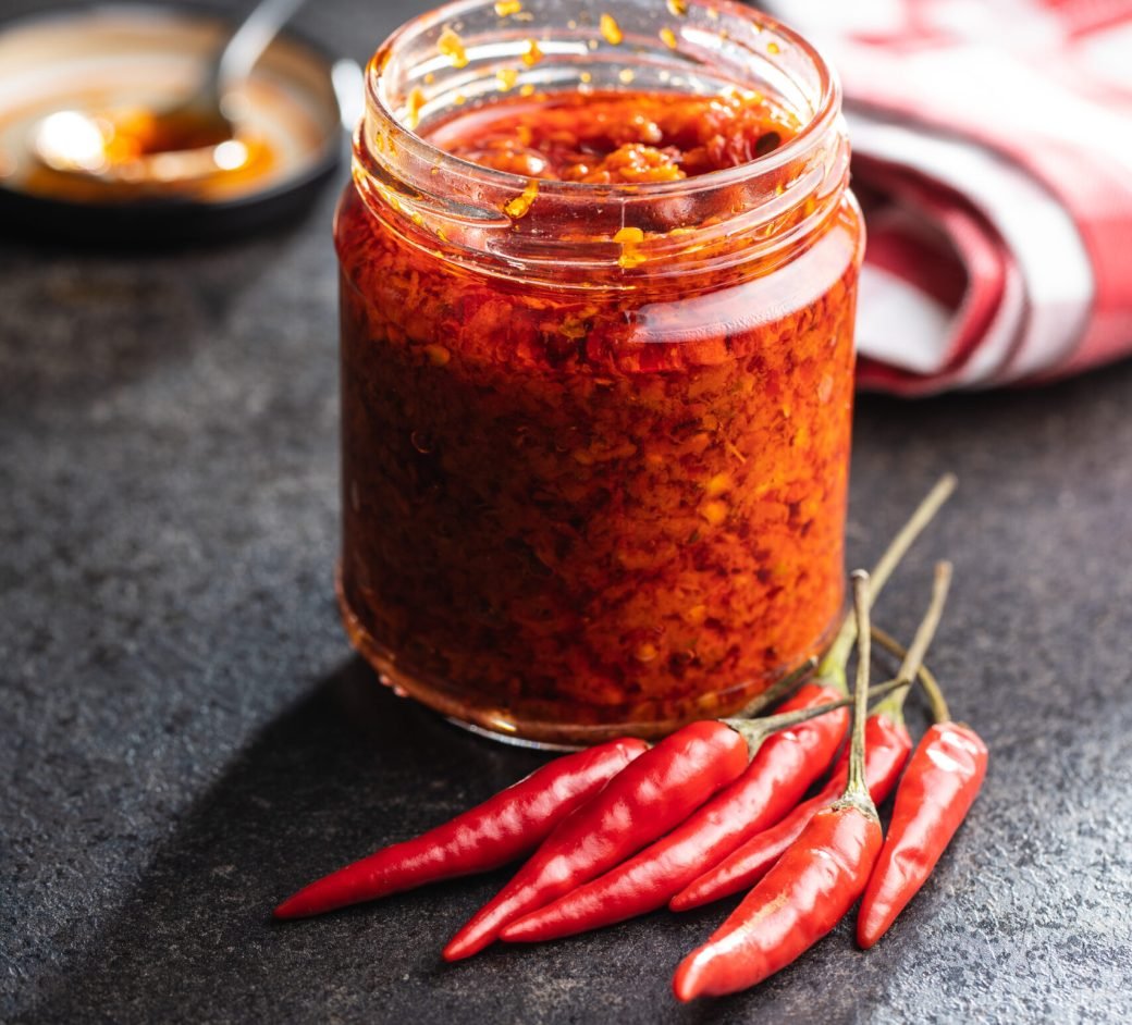 Red hot chili paste and chili pepper in jar on black table.